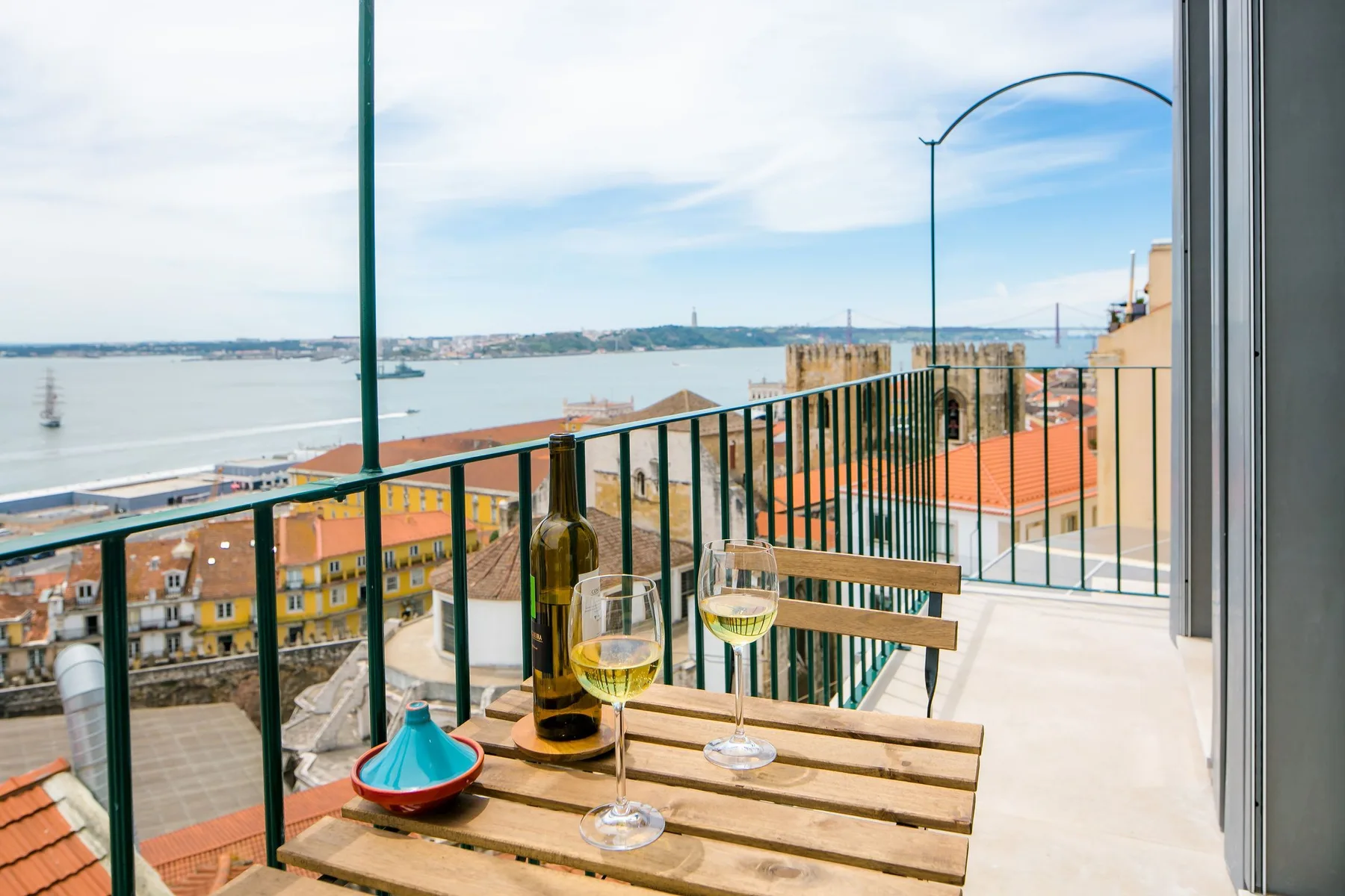 Una terraza da a la costa, con una mesa de madera y copas en primer plano.
