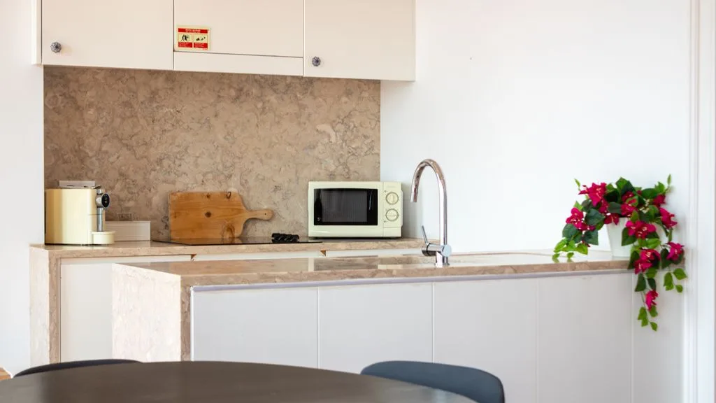 Una cocina compacta con gabinetes blancos, un microondas y flores sobre la encimera.