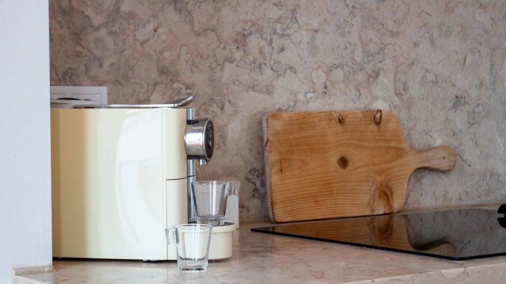 Una encimera de cocina con una cafetera, un vaso y una tabla de madera.