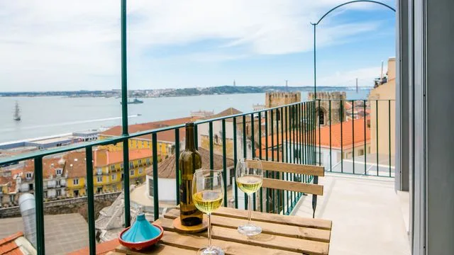 Un balcón da a la costa, con dos copas de vino sobre una mesa de madera.