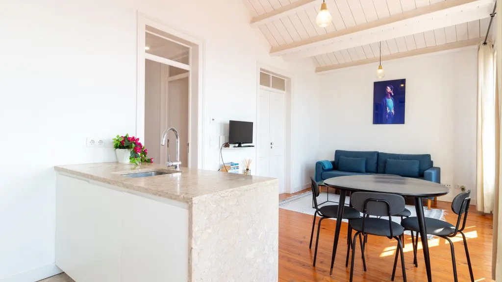 Una luminosa zona de comedor y cocina con mesa, asientos y una encimera.