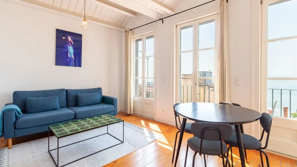 Una sala luminosa con asientos azules, una mesa de centro y ventanas altas.