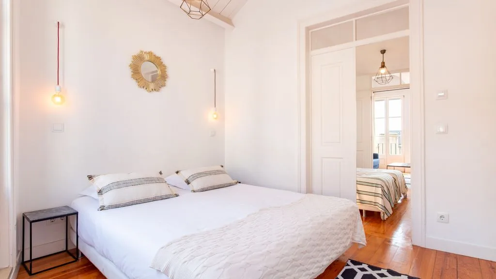 Un dormitorio luminoso con una cama doble y una puerta abierta a otra habitación.