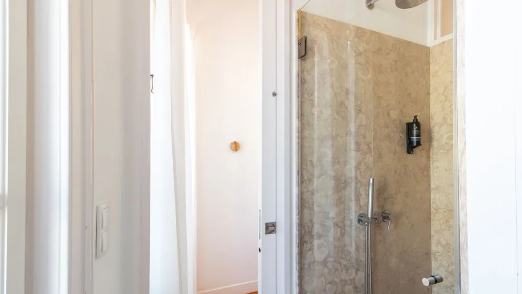 Una ducha de baño con azulejos beige y grifería cromada.
