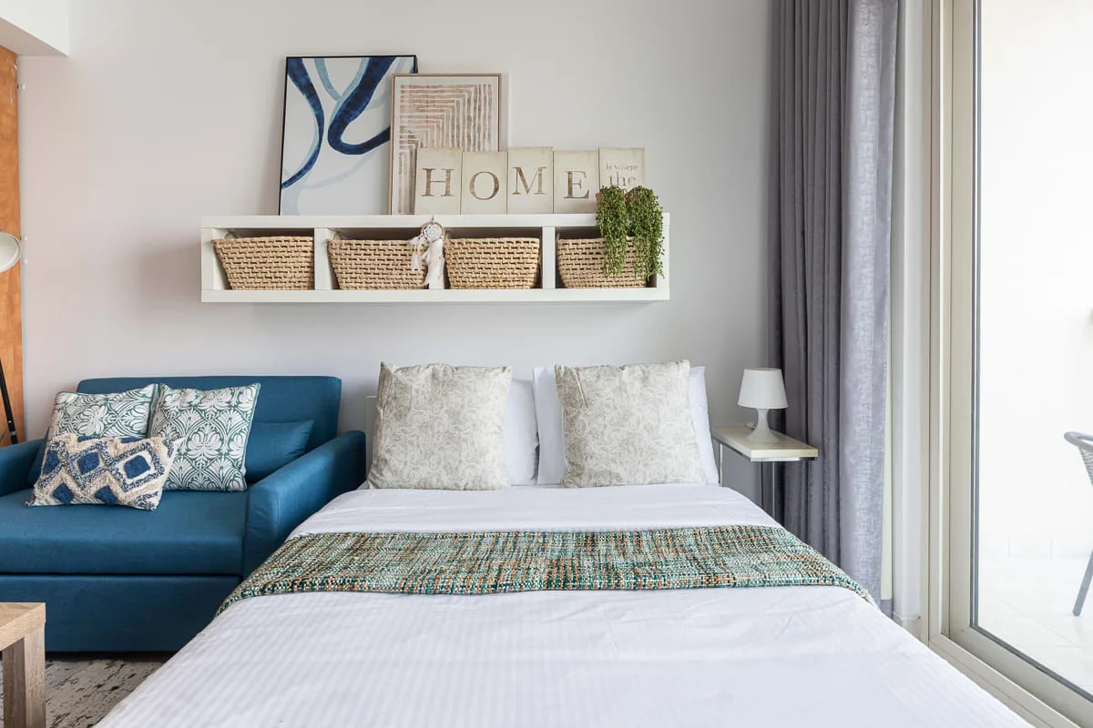 A bedroom with a neatly made bed, blue seating, and wall art.
