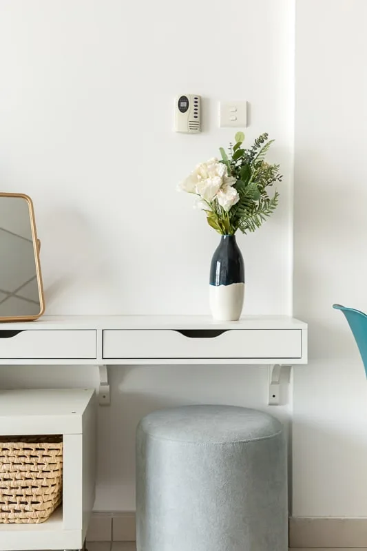 A white dressing table with a round upholstered seat and a vase of flowers.