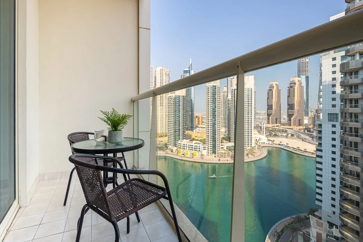 A balcony seating area overlooks a waterfront lined with high-rise buildings.