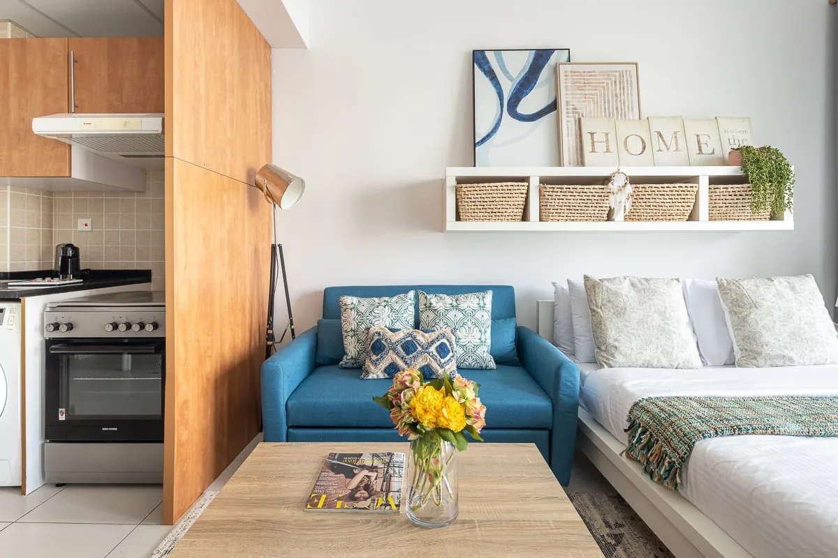 A living area with blue seating beside a bed and a wooden coffee table.