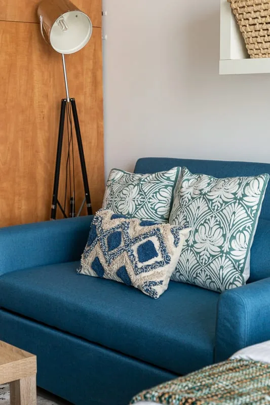 A blue sofa with patterned cushions sits beside a floor lamp.