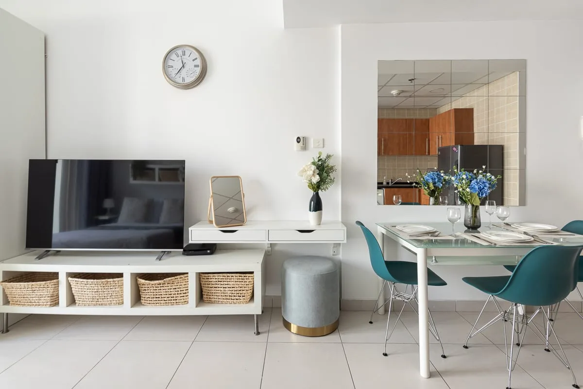 A bright living and dining area with a television, white console, and dining table.
