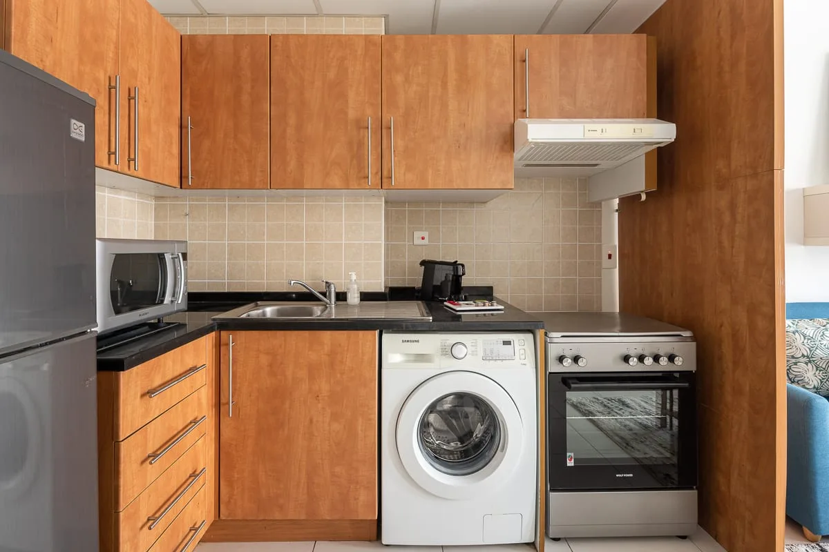 Una cocina compacta con gabinetes de madera, una lavadora y una estufa.