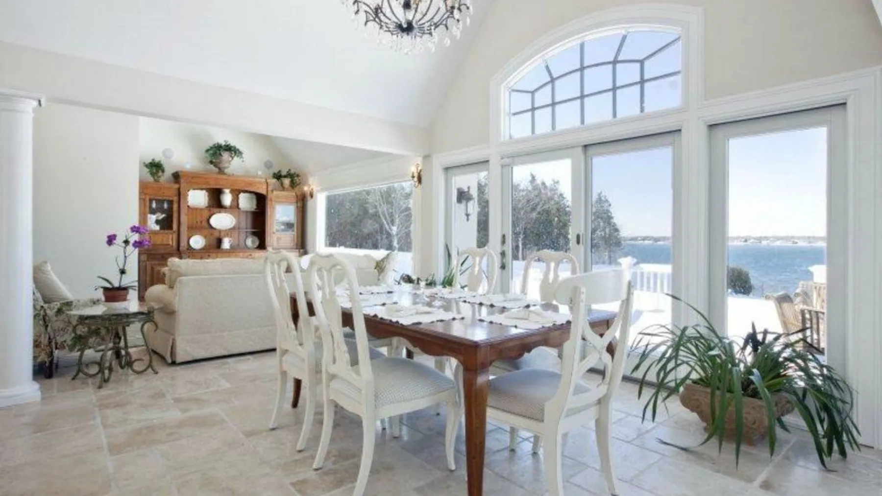 Un comedor luminoso con una mesa de madera y grandes ventanas con vistas al agua.