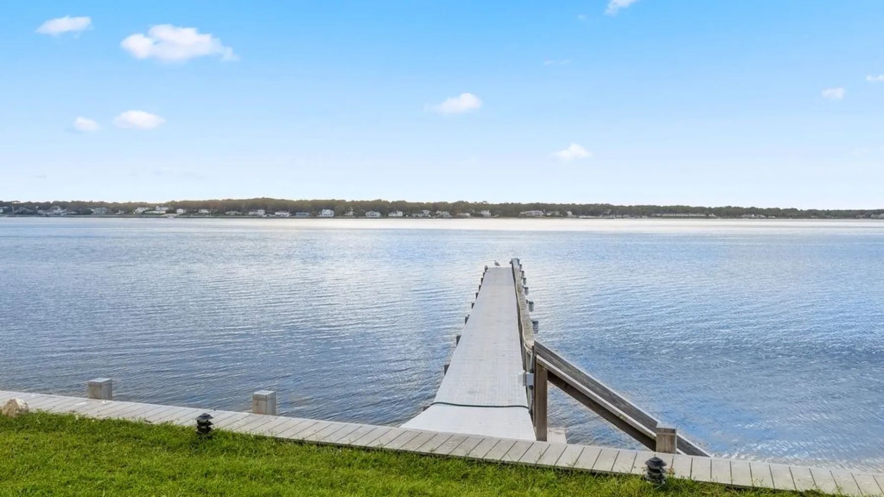 Un muelle de madera se extiende sobre aguas tranquilas hacia la orilla distante.
