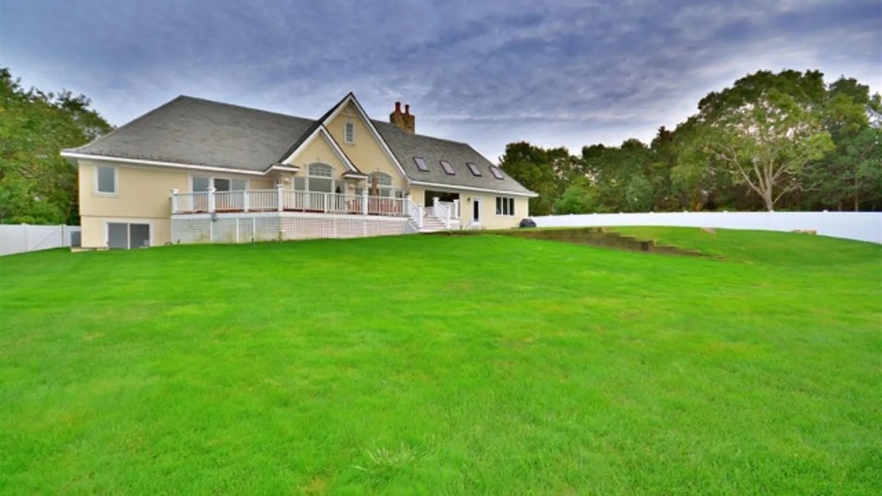 Una casa grande con balcón se alza detrás de un amplio césped verde.
