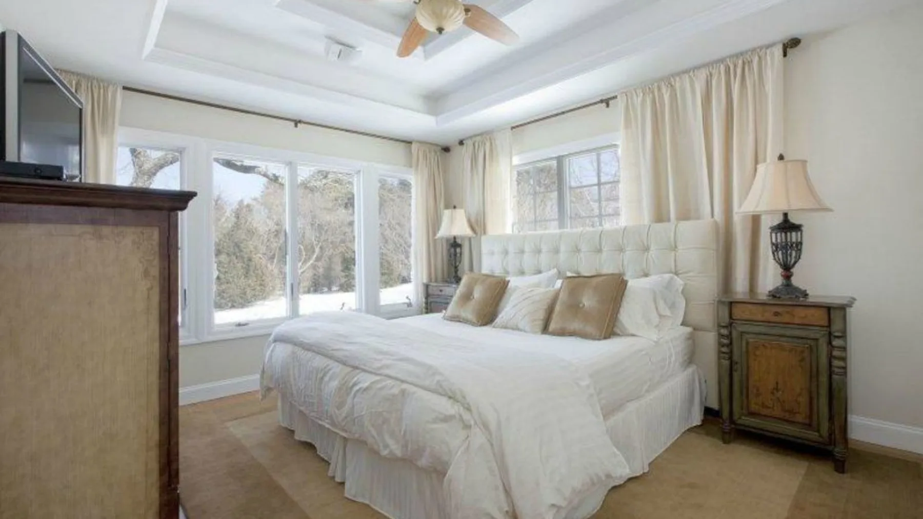 Un dormitorio luminoso con una cama blanca y grandes ventanas con cortinas.