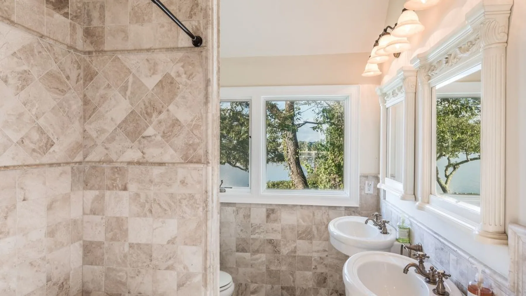 Un baño alicatado con una mampara de ducha, dos lavabos y ventanas luminosas.