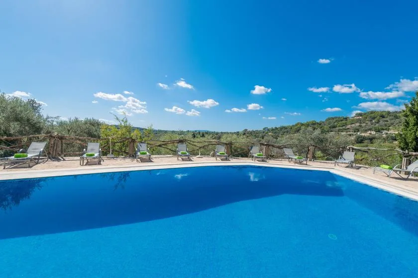 An outdoor swimming pool is surrounded by a paved deck and lounge seating.