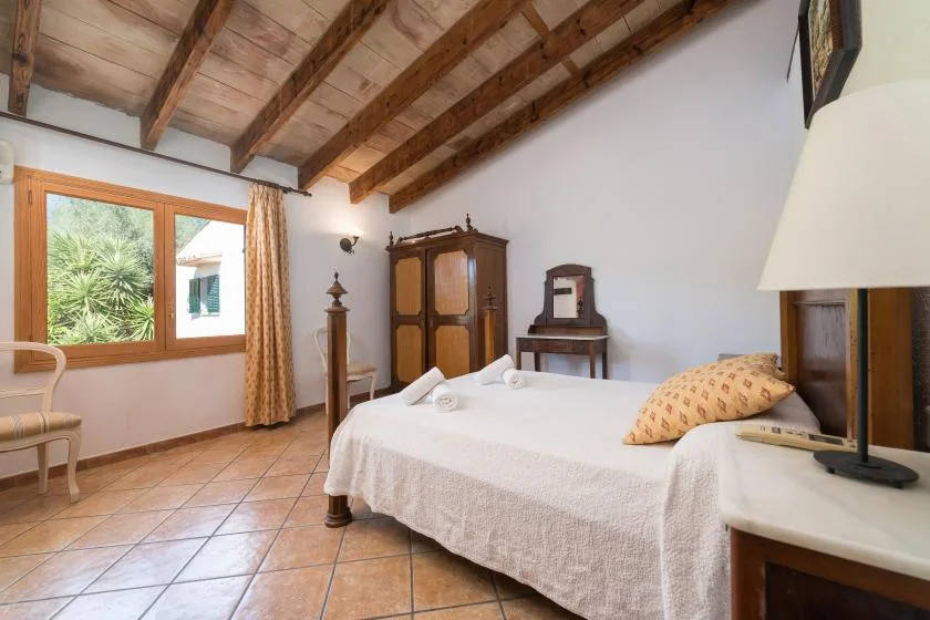 A bedroom with a neatly made bed and wooden ceiling beams.