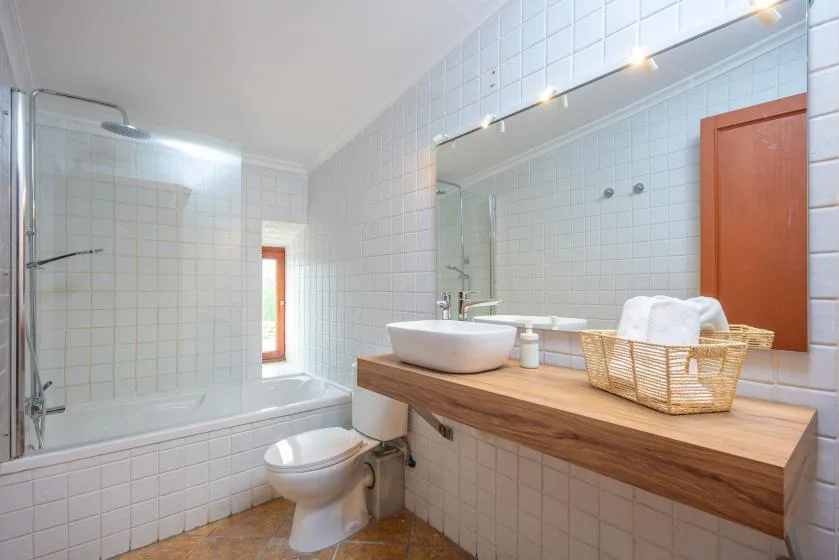 A tiled bathroom with a bathtub, toilet, and sink on a wooden counter.