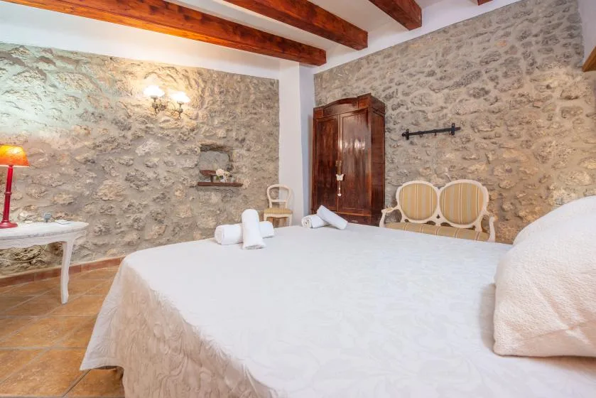 A bedroom with stone walls, exposed wooden ceiling beams, and a bed.