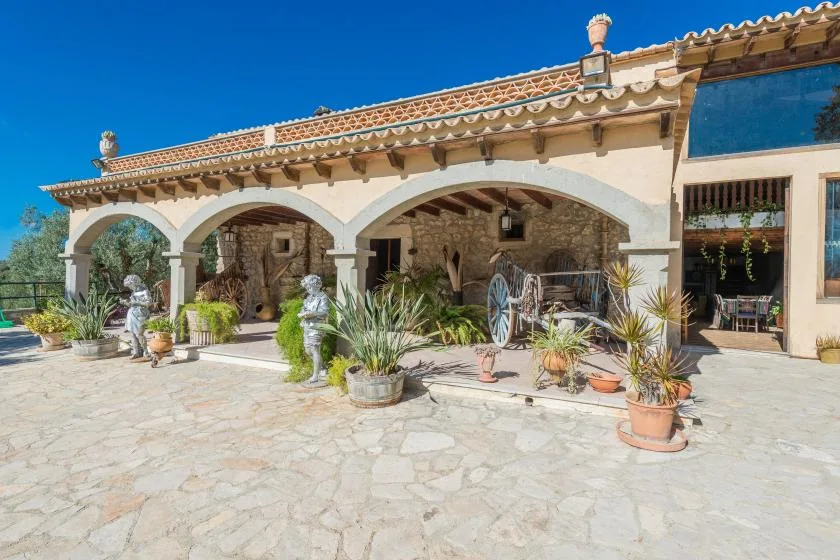 A stone-paved patio fronts a rustic building with arched openings and potted plants.