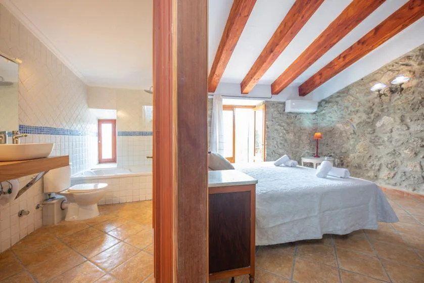 A bedroom opens onto a tiled bathroom, with exposed wooden ceiling beams.