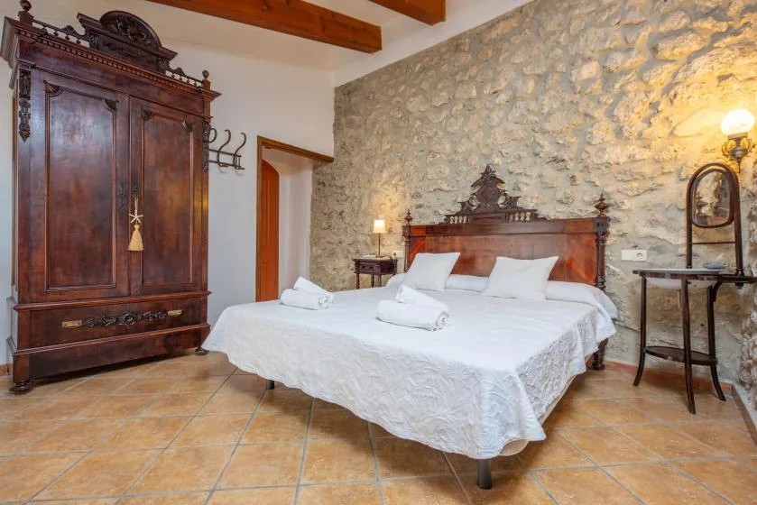 A bedroom with a double bed, white linens, and a stone wall.