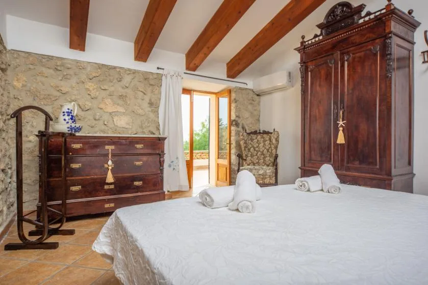 A bedroom with a white bed, antique wooden furnishings, and exposed ceiling beams.