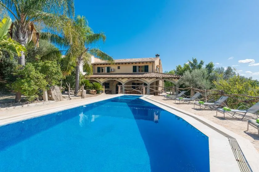 A swimming pool beside a two-story house, with lounge seating and trees.