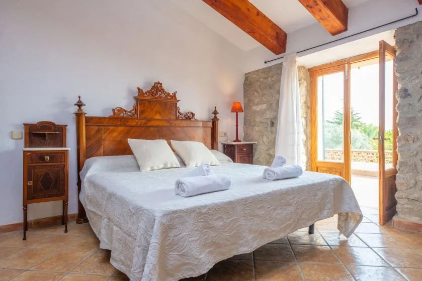 A bedroom with a neatly made bed and an open glass door to a balcony.