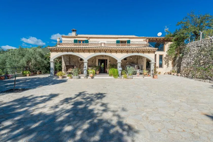 A stone-paved courtyard in front of a house with an arched veranda.