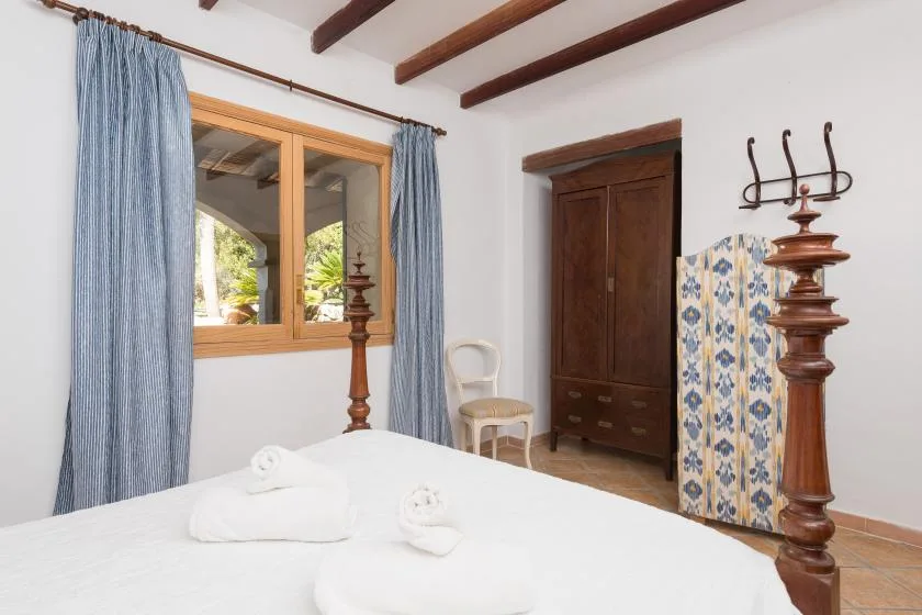 A bedroom with a wooden window, blue curtains, and a dark wooden wardrobe.