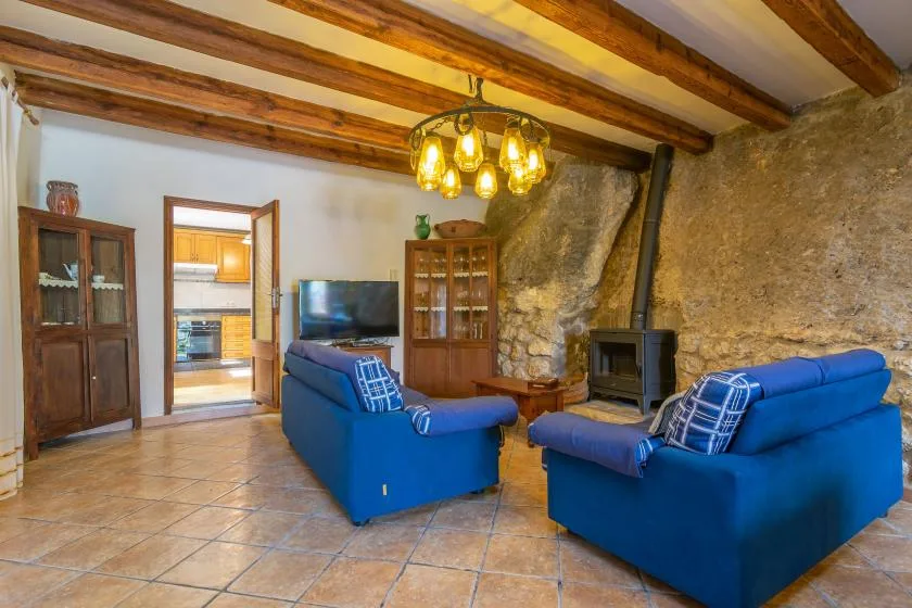 A rustic living room with blue seating, exposed ceiling beams, and a stone wall.