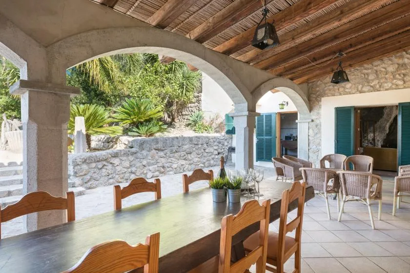 A covered patio dining area with a long table and chairs beside arched openings.