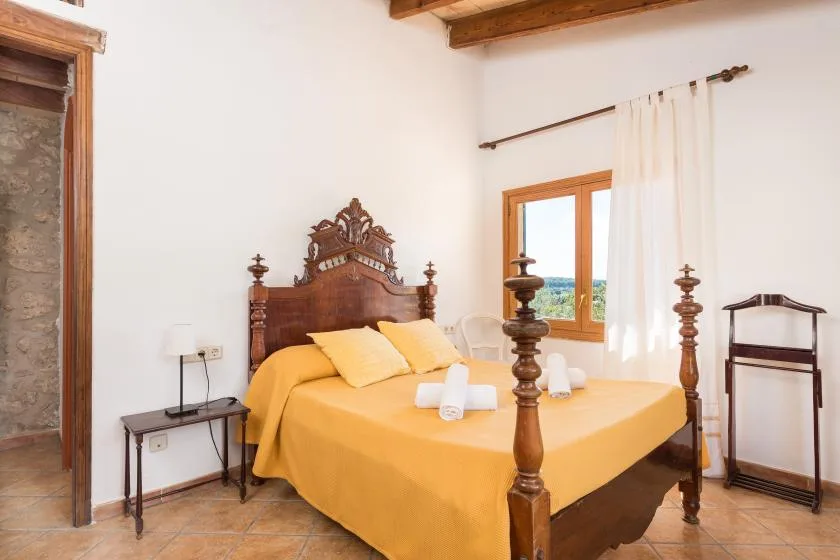 A bedroom with a large wooden bed dressed in yellow bedding beside a window.