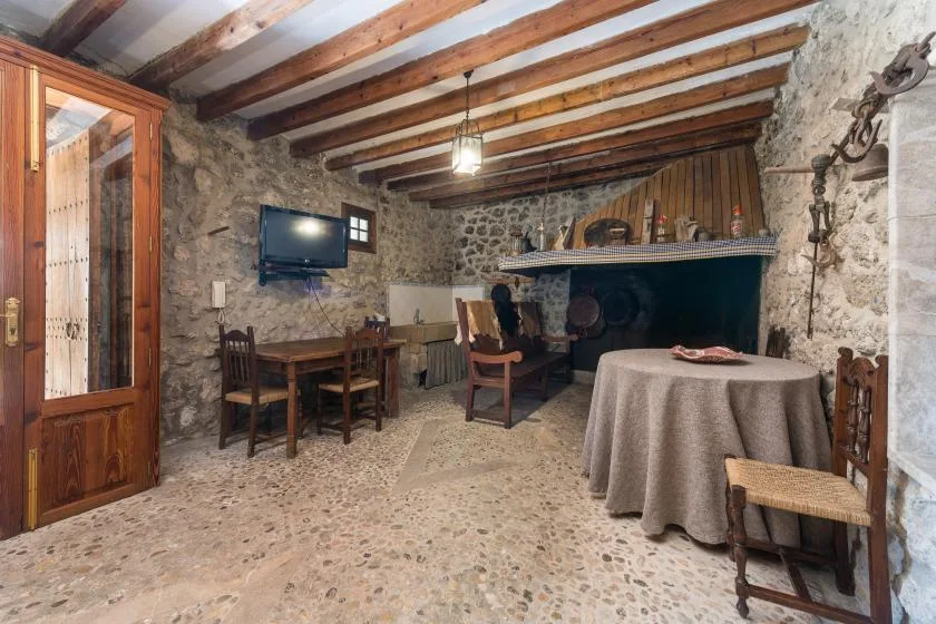 A rustic stone dining room with wooden beams and a large fireplace.