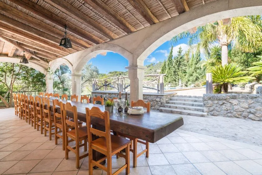 A covered outdoor dining area with a long wooden table and garden views.