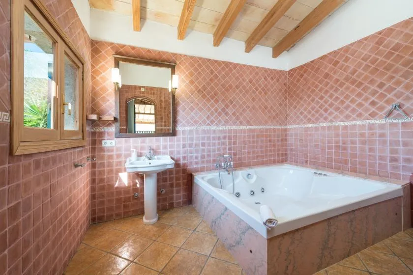 A tiled bathroom with a sink, mirror, and corner bathtub.