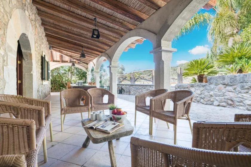 A covered stone patio with wicker seating and a low table.