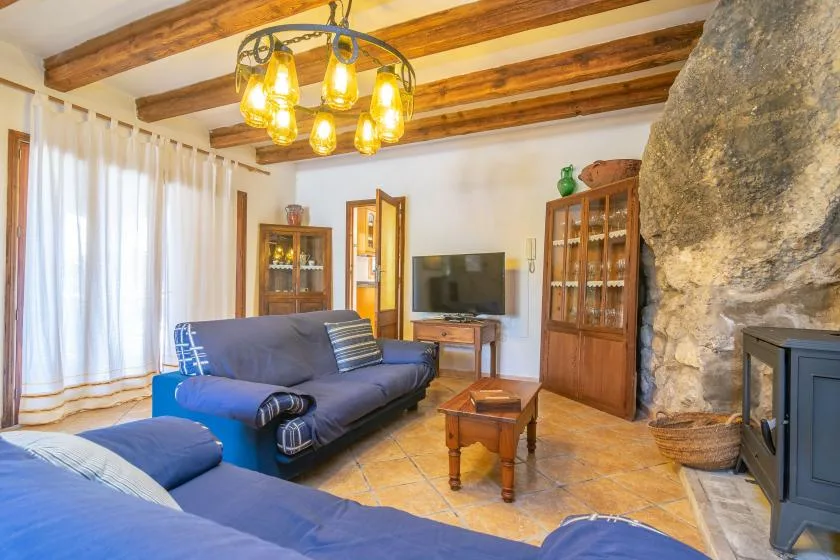 A living room with blue seating, a television, and exposed wooden ceiling beams.