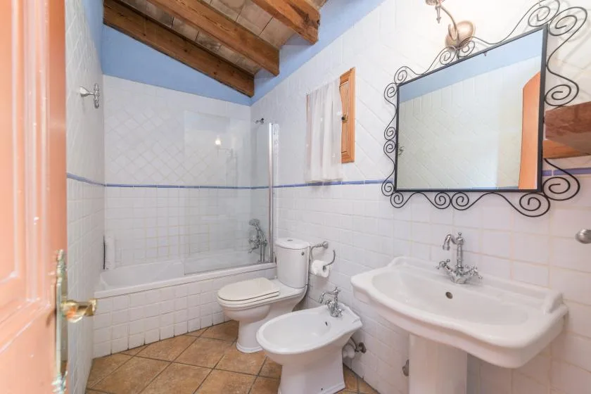 A tiled bathroom with a bathtub, toilet, bidet, and sink beneath an ornate mirror.