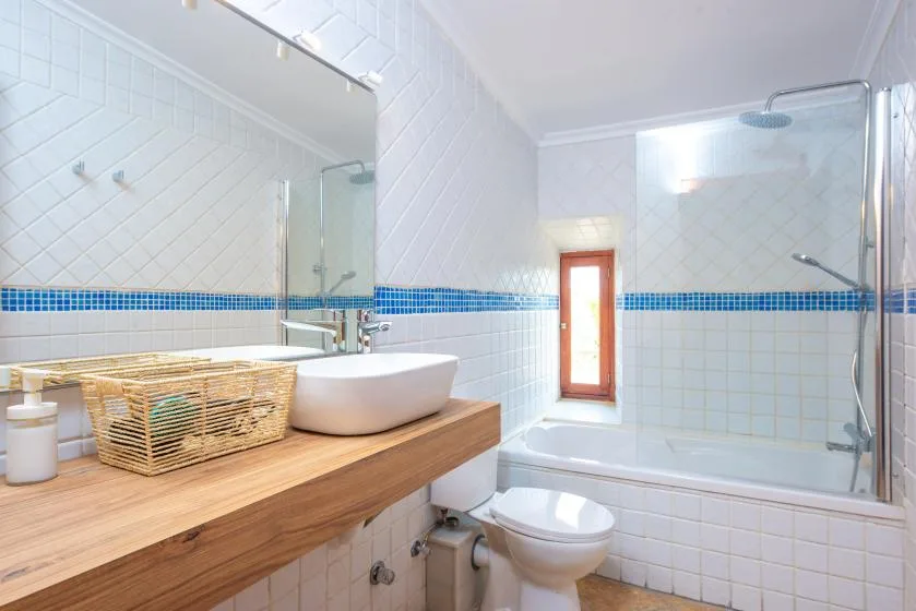 A tiled bathroom with a bathtub, shower, sink, and wooden vanity.