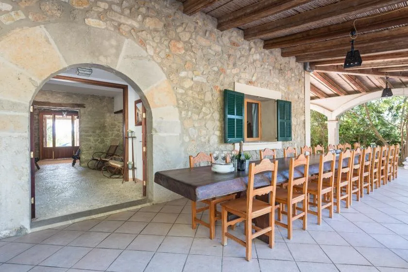 A covered stone dining area with a long wooden table and rows of chairs.