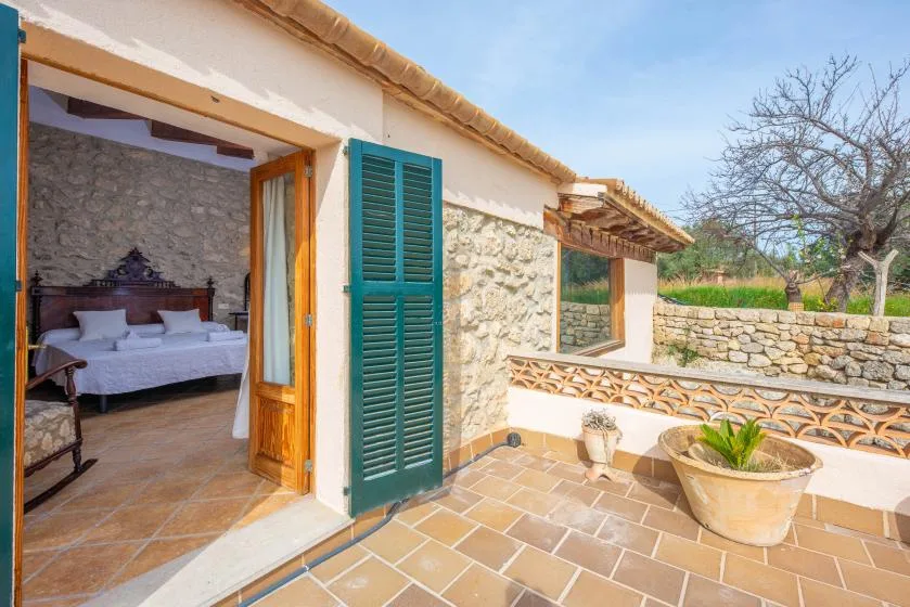 A stone house opens onto a tiled patio with a potted plant.
