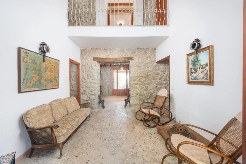 A rustic sitting room with stone walls, woven seating, and framed artwork.