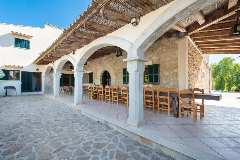 A covered outdoor dining area with arched openings and wooden tables and chairs.