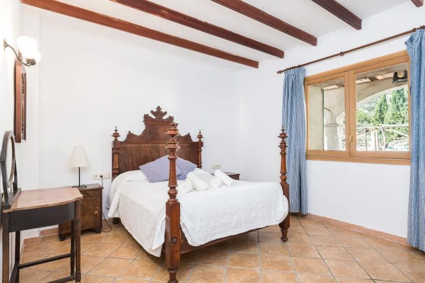 A bedroom with a wooden bed, white bedding, and a window with blue curtains.