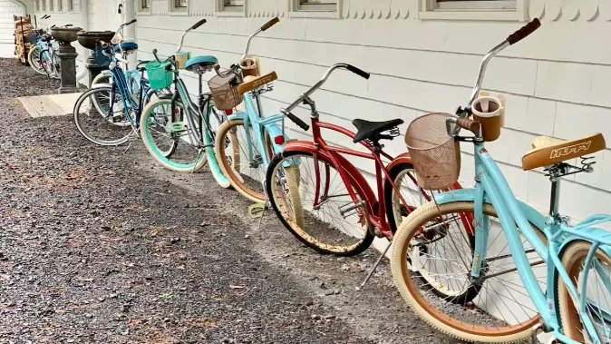 Bicycles are parked in a row beside a light-colored building.