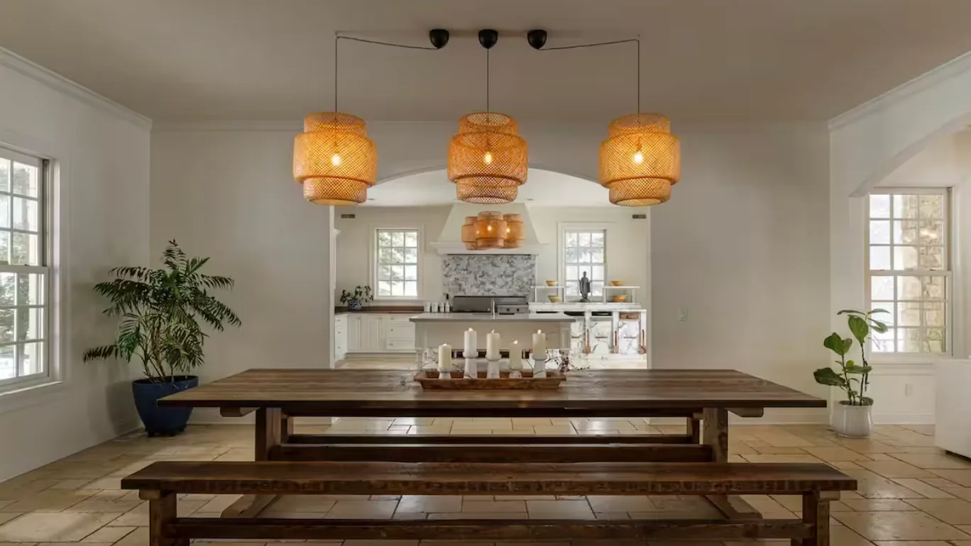 A dining room with a long wooden table beneath three pendant lights.