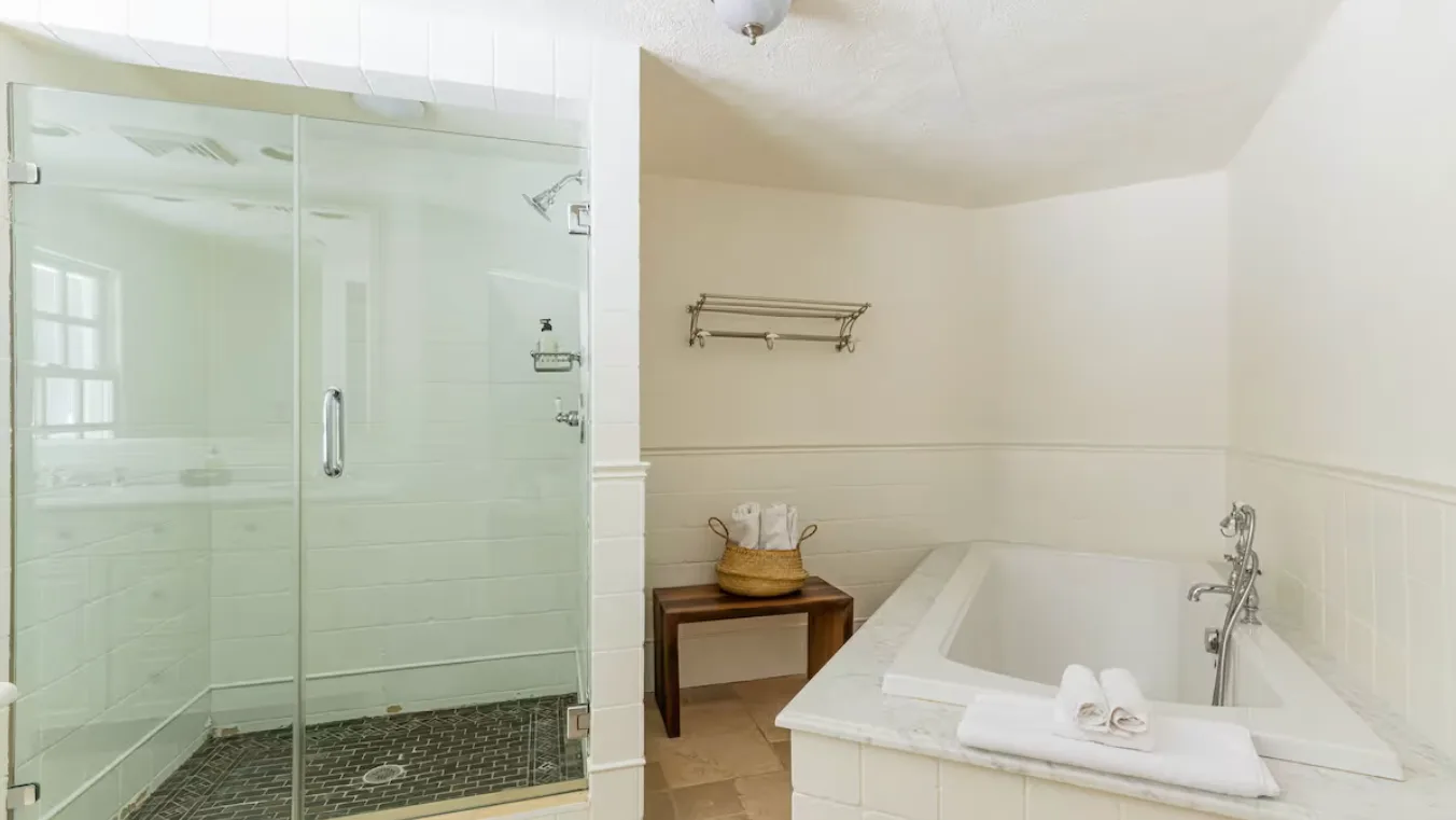 A bathroom with a bathtub, glass shower, and small wooden table.
